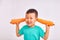 Child boy in turquoise shirt, covers ears with huge carrots - fruits and healthy food