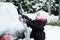 Child brushing snow off car.Kid with winter brush and scraper clearing family car