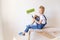 A child Builder sits on a construction ladder in an apartment with white walls and holds a felling for painting walls, a place for