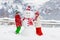 Child building snowman. Kids build snow man. Boy and girl playing outdoors on snowy winter day. Outdoor family fun on Christmas