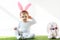 Child in bunny ears headband sitting near toy rabbit  on white