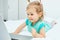 The child carefully looks into the laptop monitor while lying on the bed