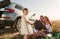 Child in center of everyone`s attention. Family have picnic at countryside near silver automobile at sunset