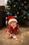 child in Christmas pajamas, Santa\\\'s hat writes letter to Santa Claus lying on floor in front of Christmas tree