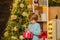 Child with a Christmas present on wooden house background. Cheerful cute child opening a Christmas present. Cute little