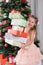 The child at Christmas tree holds boxes with gifts in hand