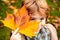 Child covers his eyes with a yellow maple leaf in the autumn park. Happy kid, little boy, playing in beautiful autumn