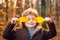 Child covers his eyes with a yellow maple leaf. Happy child laughing and playing leaves in autumn outdoors. Kids autumn
