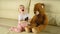 A child dances and laughs next to a toy bear in white headphones