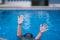 Child in danger drowning in the pool,  kid girl cannot swim to deep water and raise two hand for help on swimming pool