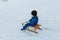 Child with dark short hair going down snowy hill on wooden sled