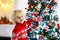 Child decorating Christmas tree at home. Little boy in knitted sweater with Xmas ornament. Family with kids celebrate winter