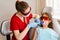 Child dentistry. Uv illumination of photopolymer tooth filling procedure. Child dentist in red protective glasses treats