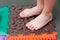 child does leg exercises on orthopedic massage mat at home. Puzzle mats imitating different textures for baby foot massage.