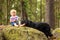 Child and dog, barefoot boy on a rock in the woods playing with a black hovie