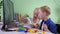 Child with Down syndrome at home education, girl helps her brother during an online lesson with teacher on screen