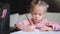 Child drawing sitting on table middle shoot. Caucasian female little girl draws with colored pencils. Female child doing