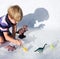 Child draws along contour contrasting shadows from figures of toy dinosaurs on light background