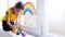 A child draws a rainbow sign of hope on a window