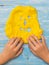 The child draws teeth on a face of yellow slime on a wooden table.