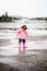 Child dressed in pink clothes jumping in puddles