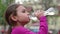 Child drinking water from bottle outdoor. Young girl with water bottle in hand