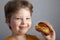 Child eats burger on grey background. Male child with hamburger