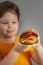 Child eats burger on grey background. Male child with hamburger