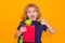 Child from elementary school with book and apple isolated on yellow background. Little student, clever nerd pupil ready