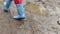 Child feet in rubber boots walk puddle dirt, construction site