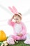 Child in funny bunny costume sitting near yellow ostrich egg, colorful Easter eggs and tulips  on white