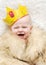 Child in a fur cape and crown on a white background. baby crying