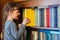 The child gets a textbook with wooden shelf of the old library. A little girl is taking a yellow book from a bookshelf. Children`