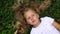 Child girl with blond hair on green grass background. A child with a smile lies on the grass in the park and smiles