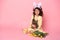 Child girl in bunny ears holding rabbit, tulips, basket with colorful eggs on pink background