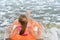 Child girl floatting on orange pool ring on the background of sea water and waves