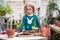 A child girl in a green dress transplants potted flowers in the winter garden. Girl in gardening help transplant flowers