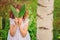 Child girl hiding behind green leaves in summer forest