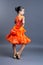 Child girl in an orange sports dress posing in dance movement on gray background
