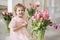 Child girl in a pink dress among tulips in vases