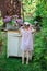 Child girl in pink plaid dress near vintage bureau with lilacs in basket