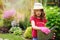 Child girl playing little gardener and helping in summer garden, wearing hat and gloves