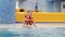 Child girl in the pool in the life jacket sits in the boiling blue water and is preparing to dive