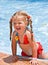 Child girl in red bikini near blue swimming pool.