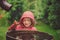 Child girl in red raincoat playing with water barrel in rainy summer garden. Water economy and nature care