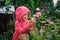 Child girl in red striped raincoat playing with wet roses in rainy summer garden. Nature care concept.