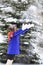 Child girl in shawl and bright blue coat stands in winter forest or Park and throws snow with hands throws snow into the air .