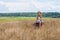 Child girl in a straw hat dress sitting on vintage suitcase and drinking tea. Cute kid with soft toy on nature lanscape