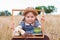 Child girl in a straw hat sitting behind vintage suitcase with cup tea. Cute kid with soft toy looking in wooden frame