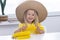 Child girl in a straw hat in yellow clothes eats corn, summer photo. on a light background.
